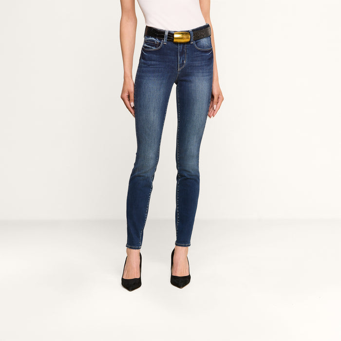 A person wearing a white top, the Marguerite Skinny Jean with a black belt, and black high heels stands against a plain white background. The Marguerite Skinny Jean is crafted from premium stretch denim for added comfort.