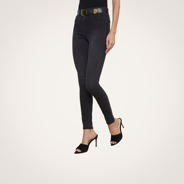 Wearing the Marguerite Skinny Jean in charcoal, styled with a black belt and black heeled sandals, a person stands against a plain light background; only their lower torso and legs are visible.