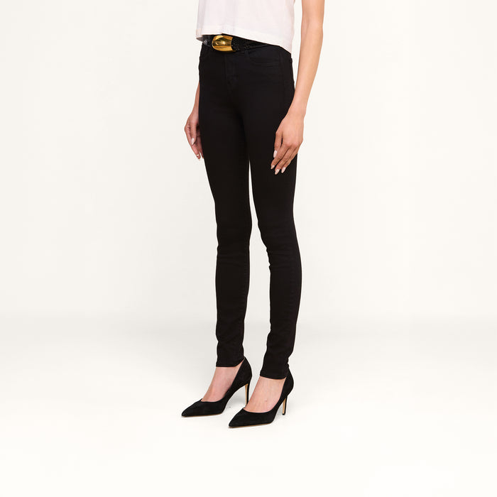 A person wearing the Marguerite Skinny Jean in black, a white top, and black high-heeled shoes stands against a plain white background.