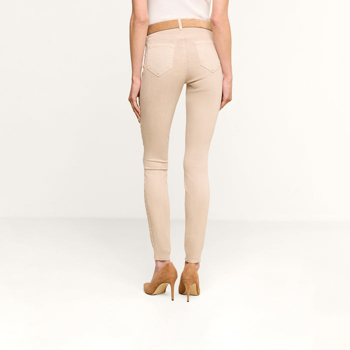 A person is shown from the back standing against a plain white background, wearing the Marguerite Skinny Jean in beige, crafted from high-recovery fabric, paired with tan high heels.