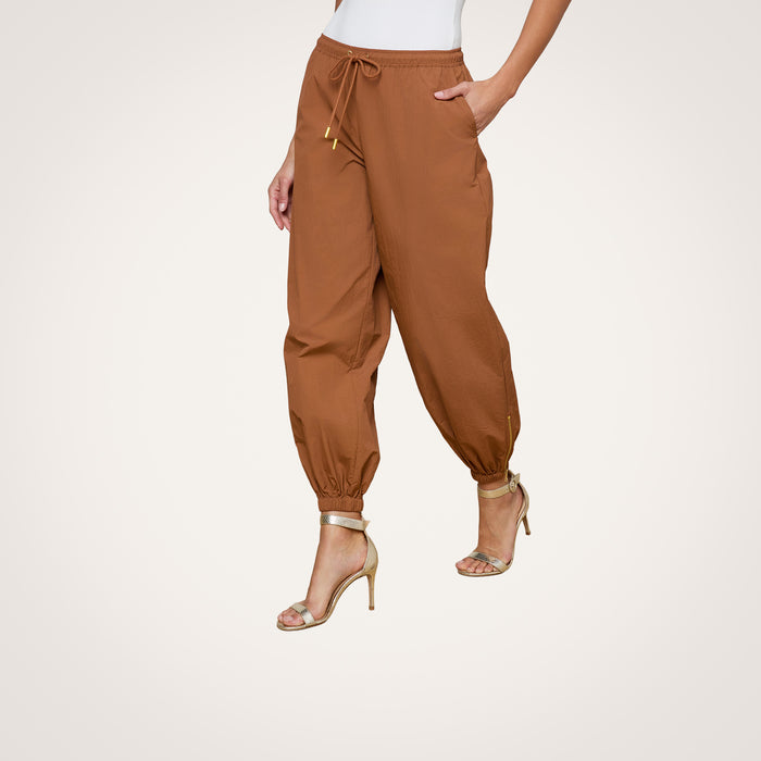 Wearing the Mariko Jogger, a modern brown jogger-style pant featuring ankle cuffs and a drawstring waist, paired with a white top and beige high-heeled sandals.