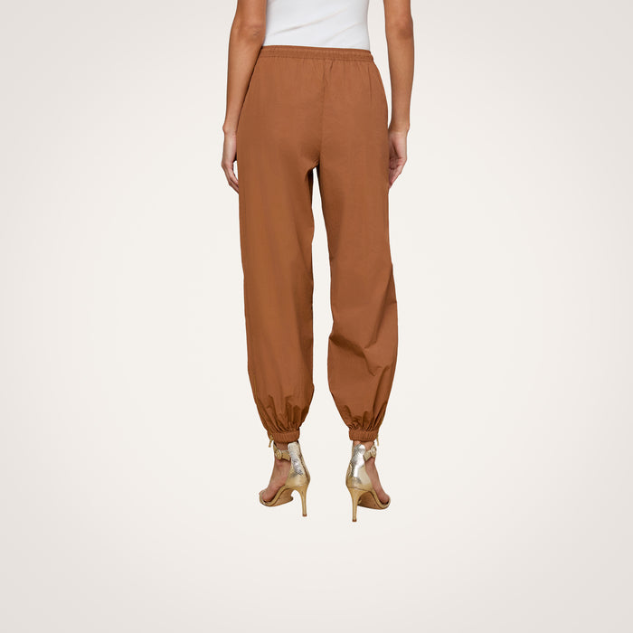A person is shown from the back against a plain light background wearing the Mariko Jogger—modern brown jogger pants crafted from water-repellent nylon—and beige high-heeled sandals.