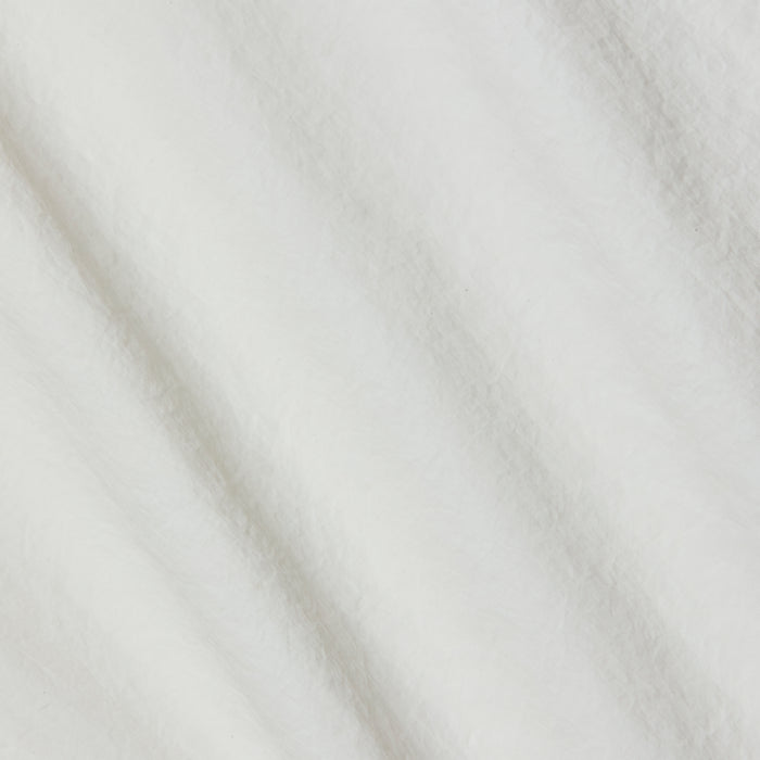 A close-up of the soft, ivory fabric of the Mariko Jogger reveals delicate texture with subtle diagonal folds and shadows. The material looks fluffy and smooth—reminiscent of fleece or cotton, yet crafted from water-repellent nylon for a modern finish.