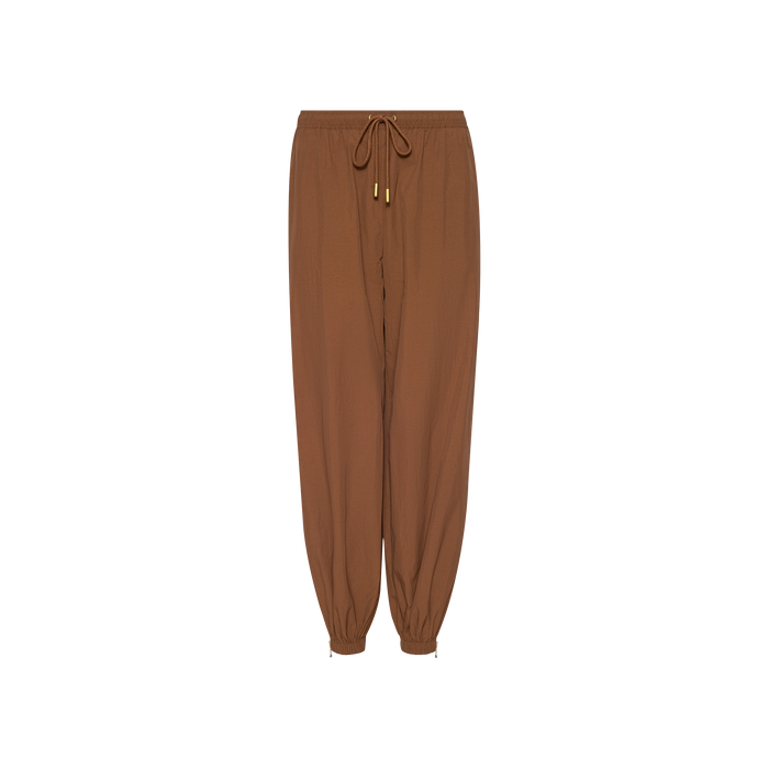 The Mariko Jogger, crafted from water-repellant nylon in brown, features a modern jogger silhouette with elastic cuffs, gold metal tips on the drawstrings, and a relaxed fit, displayed on a white background.