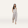 A woman stands against a plain white background, hands in pockets, wearing the Mariko Linen Jogger with a light beige sleeveless top, hoop earrings, and open-toe heels.