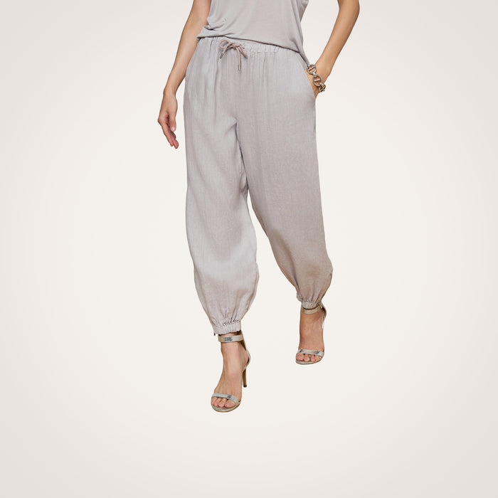 A person wearing light gray Mariko Linen Jogger pants, a matching top, and high-heeled sandals stands against a plain white background.