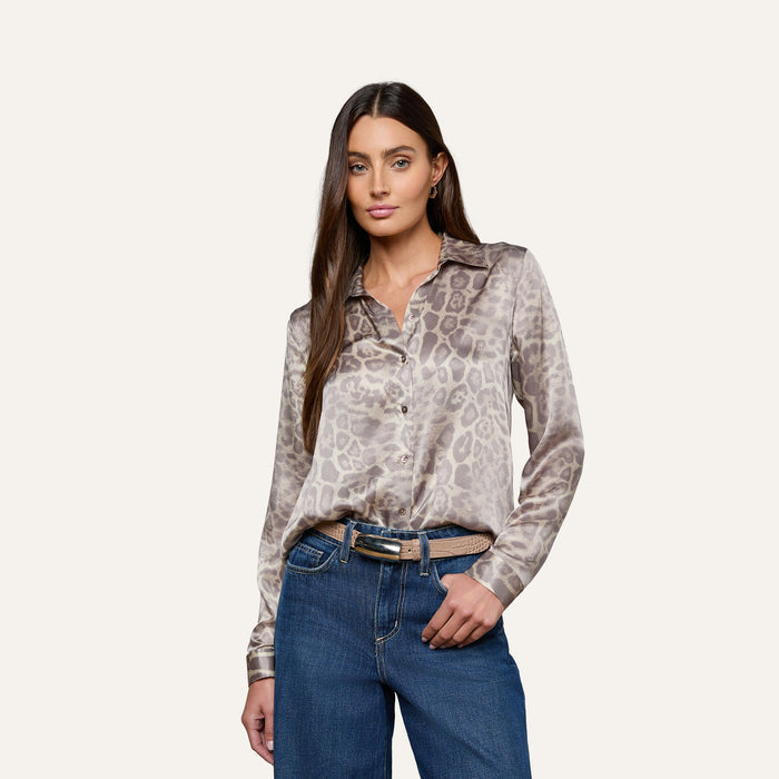 A woman stands with one hand in her pocket against a plain, light background, wearing a long-sleeve animal print blouse tucked into blue jeans and styled with the Marlowe Croc-Embossed Leather Belt.