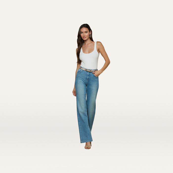 A woman stands against a plain white background wearing a white tank top, blue high-waisted wide-leg jeans, and heels, accessorized with the Marlowe Leather Belt in a python-embossed finish.