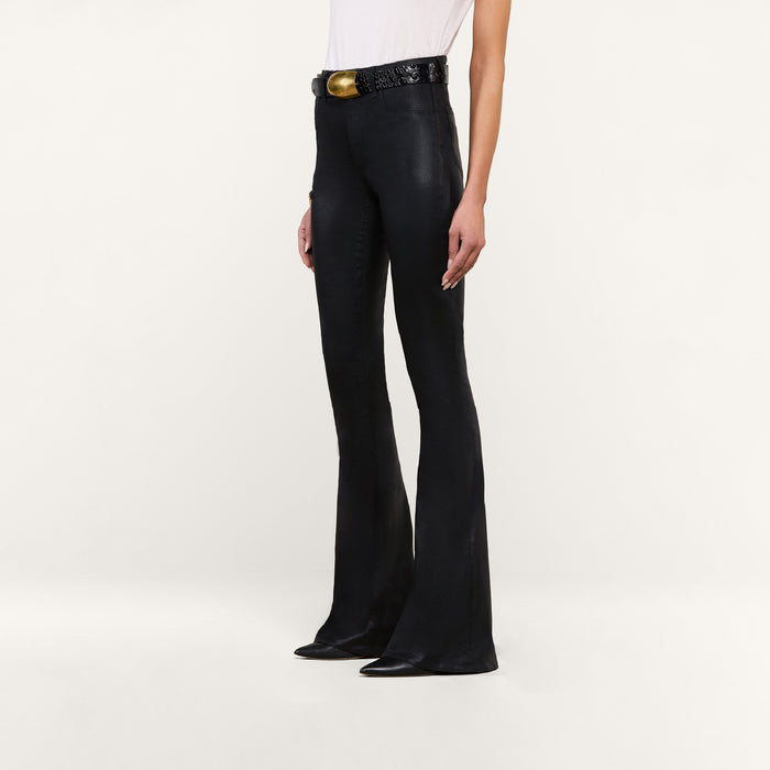 Person wearing the Marty Coated Flare Jean, styled with a black textured belt featuring a large gold buckle and a white top, standing against a plain white background. Only the lower half of their body is visible.