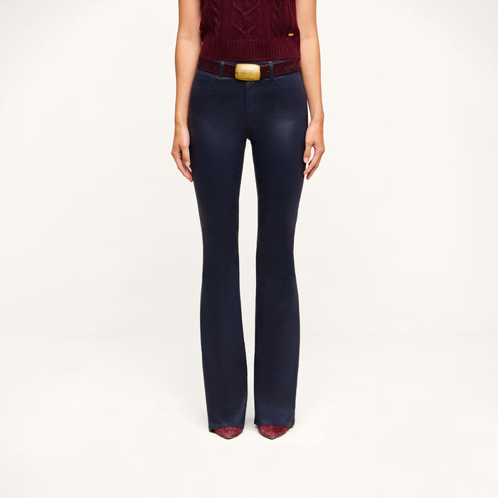 A person stands against a plain white background, visible from the shoulders down, wearing a sleeveless maroon top, maroon shoes, a brown belt with a large gold buckle, and the Marty Coated Flare Jean in dark blue with a flared hem.