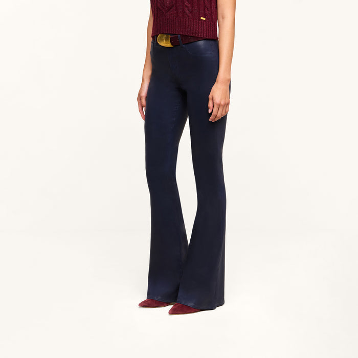 A person wearing the Marty Coated Flare Jean in dark blue, paired with a red sweater and red pointed shoes, stands against a plain white background. Only the lower torso and legs are visible.