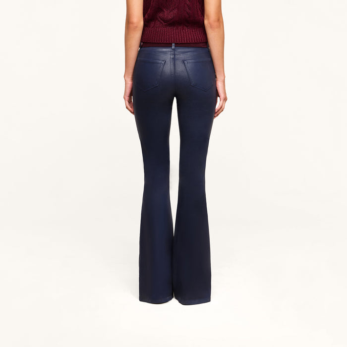 A person is standing facing away against a plain light background, wearing the Marty Coated Flare Jean with a flared hem and paired with a sleeveless maroon top, their arms relaxed at their sides.