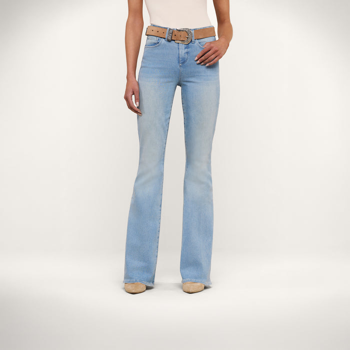 A person wearing Marty Flare Jean in light blue—a high rise, flare-leg style crafted from super stretch denim—paired with a tan belt, beige shoes, and a sleeveless top stands against a plain white background. Only the lower torso and legs are visible.