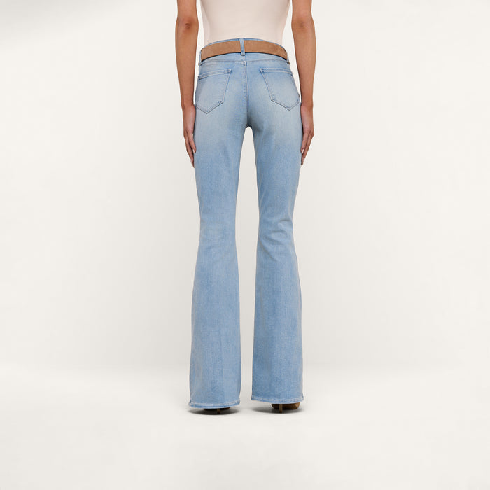 A person wearing the Marty Flare Jean in light blue with a beige top, shown from the back and standing against a plain white background.
