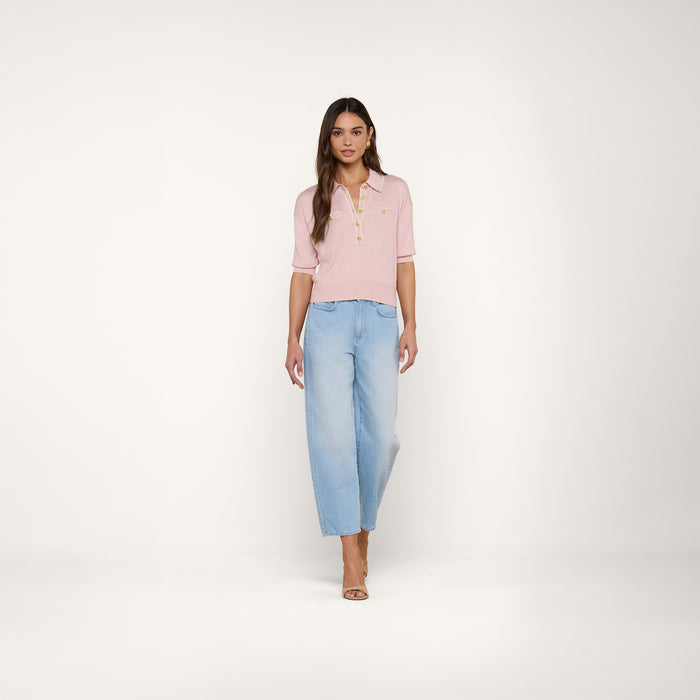 A woman stands facing forward, wearing the Masaki Cropped Sweater in light pink paired with light blue wide-leg jeans. She has long brown hair and is wearing open-toe heels against a plain white background.