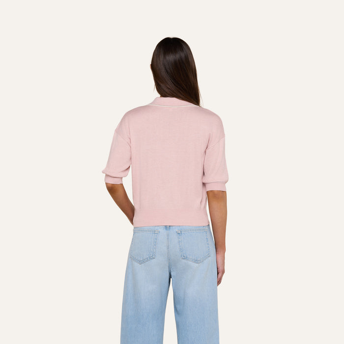 A person with long brown hair is shown from the back against a plain light background, wearing the Masaki Cropped Sweater in light pink and light blue jeans.