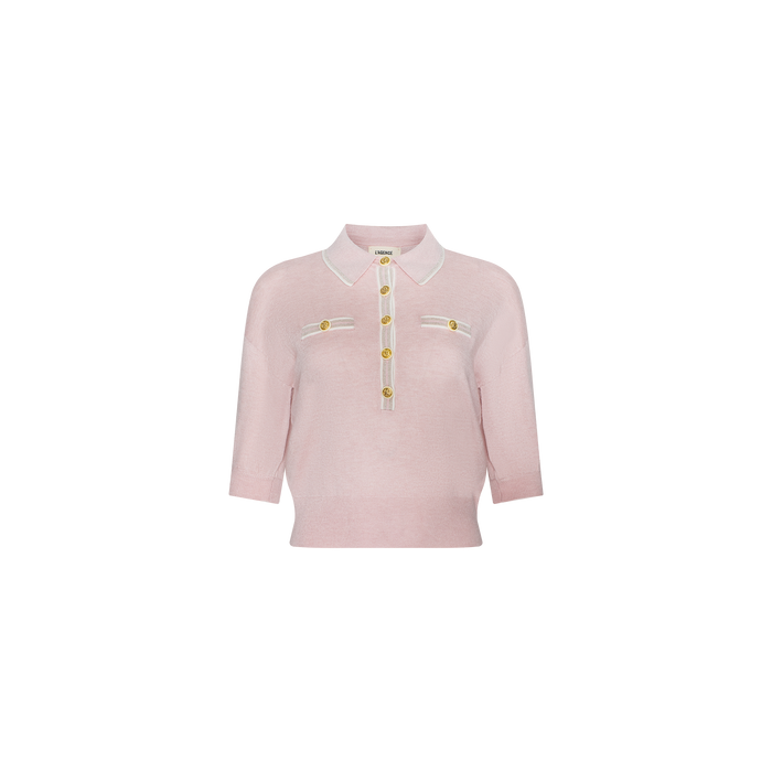 The Masaki Cropped Sweater is a light pink, featherweight knit polo top with short sleeves, a white-trimmed collar, four gold buttons down the front, and two chest pockets adorned with matching buttons. This shirt features a fitted silhouette.