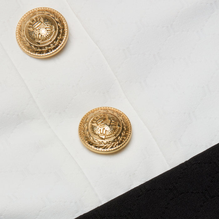 Close-up of two gold decorative buttons with an eagle emblem on the Mila One-Piece Swimsuit, set against textured white fabric with a black border at the bottom right corner, evoking a touch of French glamour.