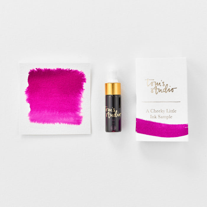 A mini ink sample bottle of Raspberry Sorbet pink fountain pen ink by Tom’s Studio, displayed alongside a swatch of the ink on textured paper and its matching packaging. The bottle is small, with a gold cap and a white pipette dropper, and features 'Tom’s Studio' in gold lettering. The ink swatch shows a rich, shimmering hue with a gradient from deep to lighter tones. The packaging, a small white card, has 'Tom’s Studio' embossed in gold at the top, with a brushstroke of the ink colour at the bottom.