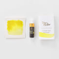 A mini ink sample bottle of Lemon Yellow fountain pen ink by Tom’s Studio, displayed alongside a swatch of the ink on textured paper and its matching packaging. The bottle is small, with a gold cap and a white pipette dropper, and features 'Tom’s Studio' in gold lettering. The ink swatch shows a rich, shimmering hue with a gradient from deep to lighter tones. The packaging, a small white card, has 'Tom’s Studio' embossed in gold at the top, with a brushstroke of the ink colour at the bottom.