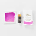 A mini ink sample bottle of Cherry Bomb pink shimmer fountain pen ink by Tom’s Studio, displayed alongside a swatch of the ink on textured paper and its matching packaging. The bottle is small, with a gold cap and a white pipette dropper, and features 'Tom’s Studio' in gold lettering. The ink swatch shows a rich, shimmering hue with a gradient from deep to lighter tones. The packaging, a small white card, has 'Tom’s Studio' embossed in gold at the top, with a brushstroke of the ink colour at the bottom.