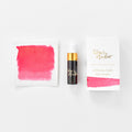 A mini ink sample bottle of Watermelon pink shimmer fountain pen ink by Tom’s Studio, displayed alongside a swatch of the ink on textured paper and its matching packaging. The bottle is small, with a gold cap and a white pipette dropper, and features 'Tom’s Studio' in gold lettering. The ink swatch shows a rich, shimmering hue with a gradient from deep to lighter tones. The packaging, a small white card, has 'Tom’s Studio' embossed in gold at the top, with a brushstroke of the ink colour at the bottom.