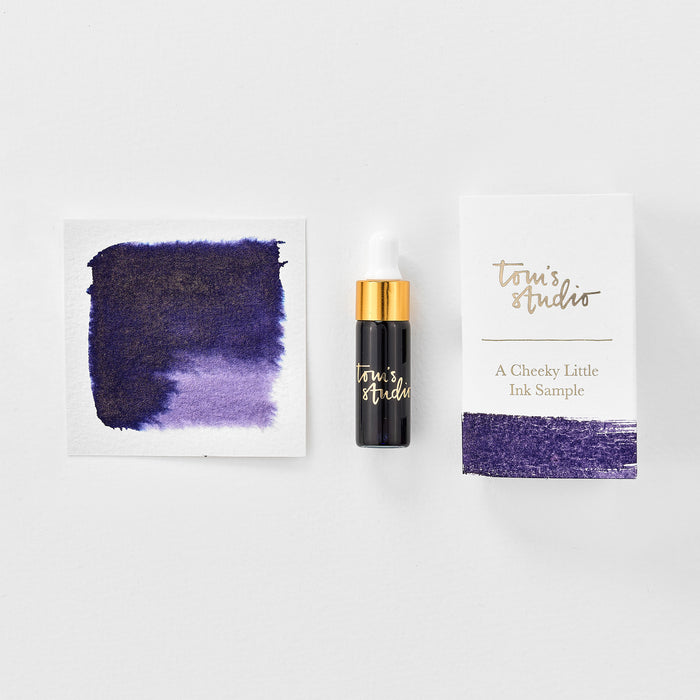 A mini ink sample bottle of Broadway purple shimmer fountain pen ink by Tom’s Studio, displayed alongside a swatch of the ink on textured paper and its matching packaging. The bottle is small, with a gold cap and a white pipette dropper, and features 'Tom’s Studio' in gold lettering. The ink swatch shows a rich, shimmering hue with a gradient from deep to lighter tones. The packaging, a small white card, has 'Tom’s Studio' embossed in gold at the top, with a brushstroke of the ink colour at the bottom.