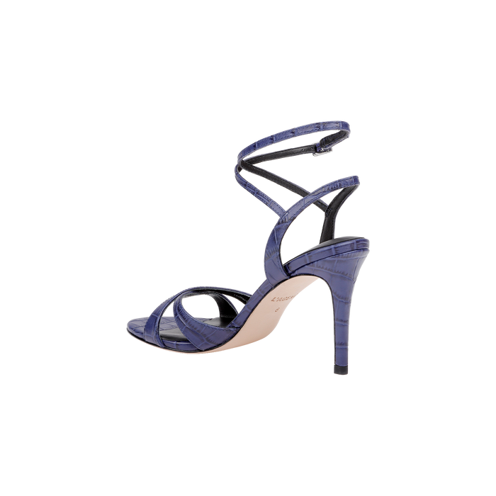 The Miranda Leather Sandal is a high-heeled sandal crafted in glossy purple leather with a crocodile texture, showcasing crisscross straps and an ankle-wrap closure, displayed from the side against a white background. Perfect for complementing evening gowns.