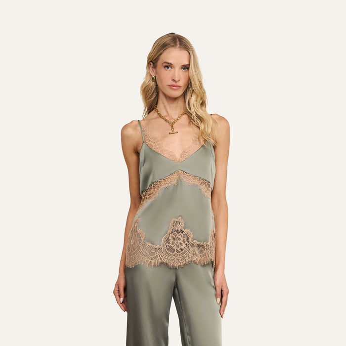 A woman with long blonde hair wears the Mitsu Satin Lace Camisole in light green, paired with matching pants featuring tan lace trim, while standing against a plain white background. The lingerie-inspired top adds an elegant touch to her outfit.