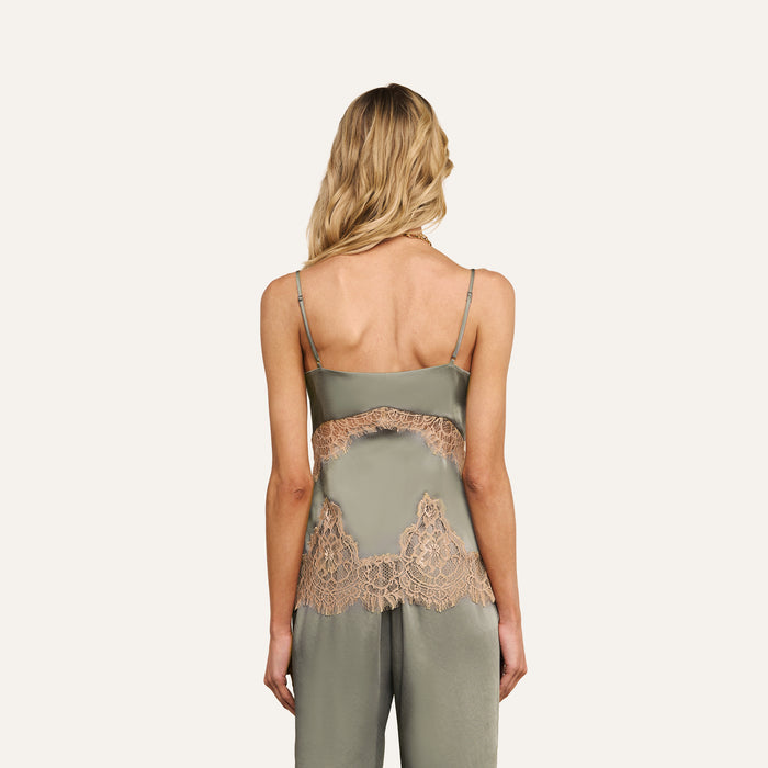 A woman with long blonde hair is shown from the back wearing the Mitsu Satin Lace Camisole, a lingerie-inspired satin pajama top featuring lace trim and spaghetti straps in a light olive color.