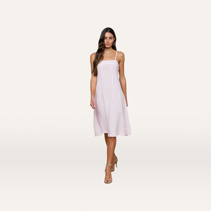 Woman wearing the Mitzy Linen Midi Dress, a sleeveless light pink linen day dress with adjustable straps, paired with beige high heel sandals, standing against a plain white background.