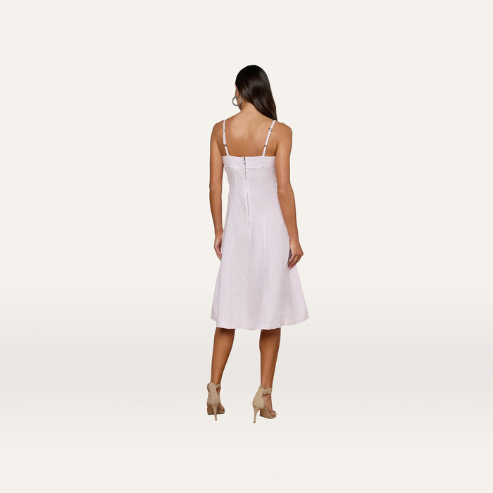 A woman stands facing away, wearing the Mitzy Linen Midi Dress in light pink with adjustable straps, paired with beige high-heeled sandals against a plain, light background.