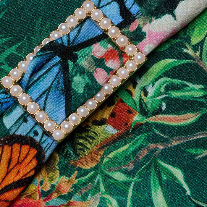 The Miya Bikini Bottom features a colorful fabric with a butterfly floral print, including leaves, butterflies, and an umbrella motif, and is adorned with a decorative rectangular pearl brooch.