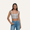 A woman wearing the Muno Tweed Top—a sleeveless, cropped style with frayed edges and large buttons—paired with light blue high-waisted jeans, stands against a plain light background.