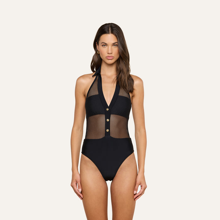 A woman stands against a plain light background wearing the Natalya Collared One-Piece Swimsuit—a chic French design in black mesh featuring a plunging neckline, mesh panels, three front buttons, and UPF 50 protection.