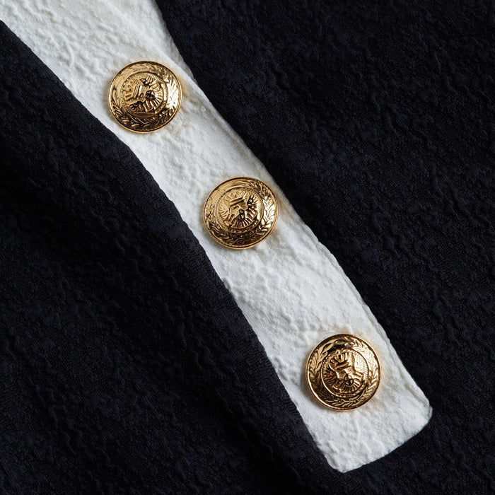 Close-up of three ornate gold buttons on the textured bouclé fabric of the Natalya Collared One-Piece, with a white stripe running underneath. The buttons feature an embossed crest design, highlighting the refined details that define this chic swimsuit.