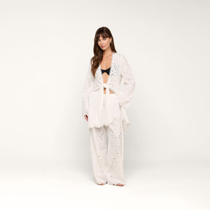 A woman stands against a plain white background wearing the Navaeh Cover-Up Kimono layered over a black bralette and matching wide-leg pants. Her hair is down, and she looks calmly at the camera.