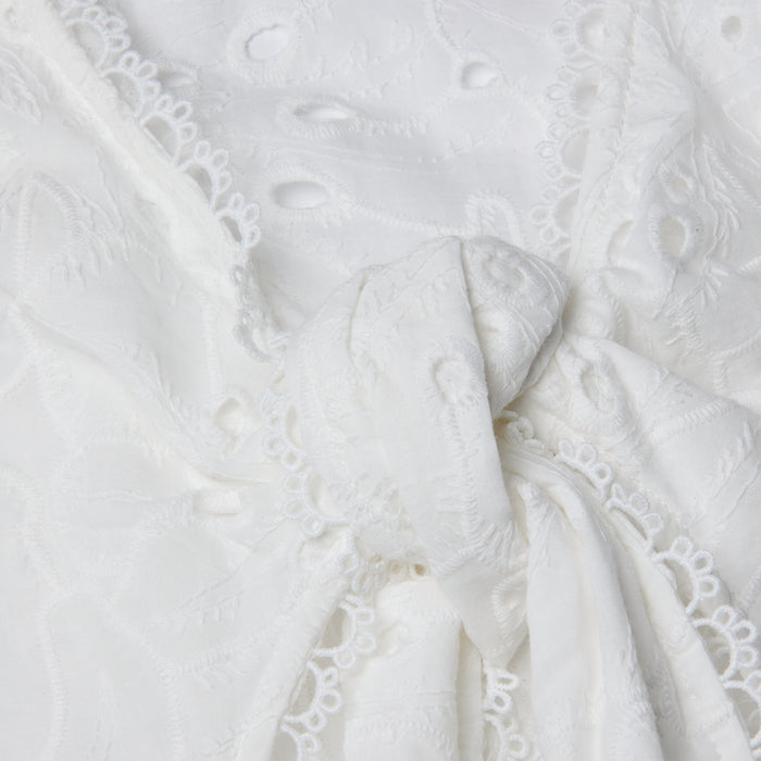 Close-up of the Navaeh Cover-Up Kimono, featuring white embroidered lace fabric tied in a knot, with delicate floral patterns and scalloped edges reminiscent of lightweight cotton eyelet.