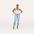A woman stands with hands on hips, wearing a white tank top and the Nevia Slouchy Straight-Leg Jean in a light wash with rolled cuffs, paired with a belt and heeled sandals against a plain, light background.