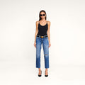 A woman in sunglasses, a black tank top, and the Nevia Slouchy Straight-Leg Jean—vintage-inspired, blue, ripped, and crafted from all-cotton denim—styled with a black belt and black heels stands against a plain white background.