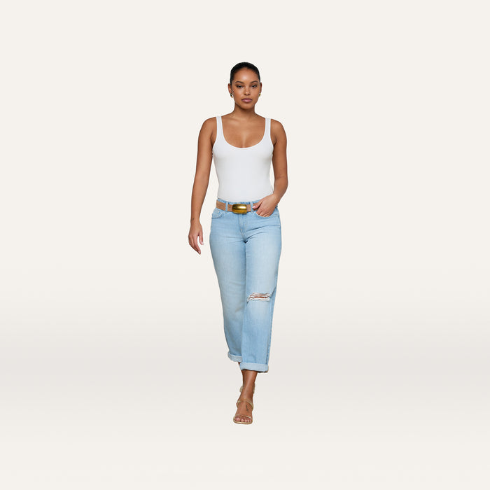 Woman in a white tank top, Nevia Slouchy Straight-Leg Jean in a light wash with rips, and brown sandals walks forward with a confident expression against a plain white background.