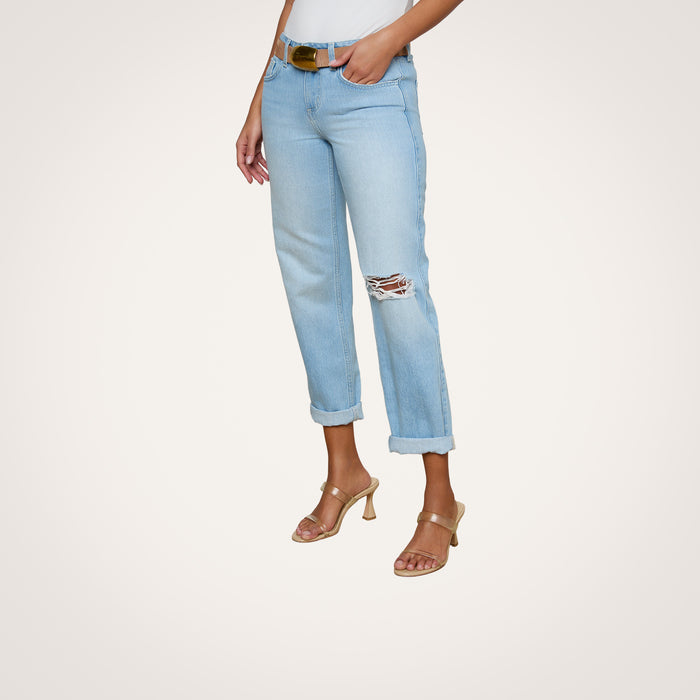 Wearing the Nevia Slouchy Straight-Leg Jean in vintage-inspired light blue with a knee rip and cuffed hems, a person pairs the jeans with a white top, a brown belt, and beige heeled sandals while standing against a plain background.