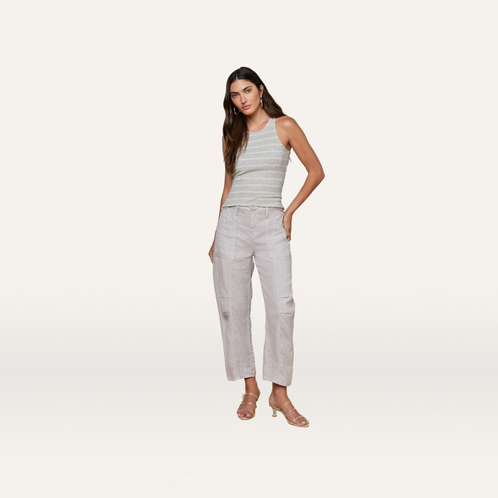 A woman stands against a plain white background, wearing the Nia Ribbed Tank, light-colored cropped pants, and open-toe heels. She has long dark hair and is posing with one hand in her pocket.