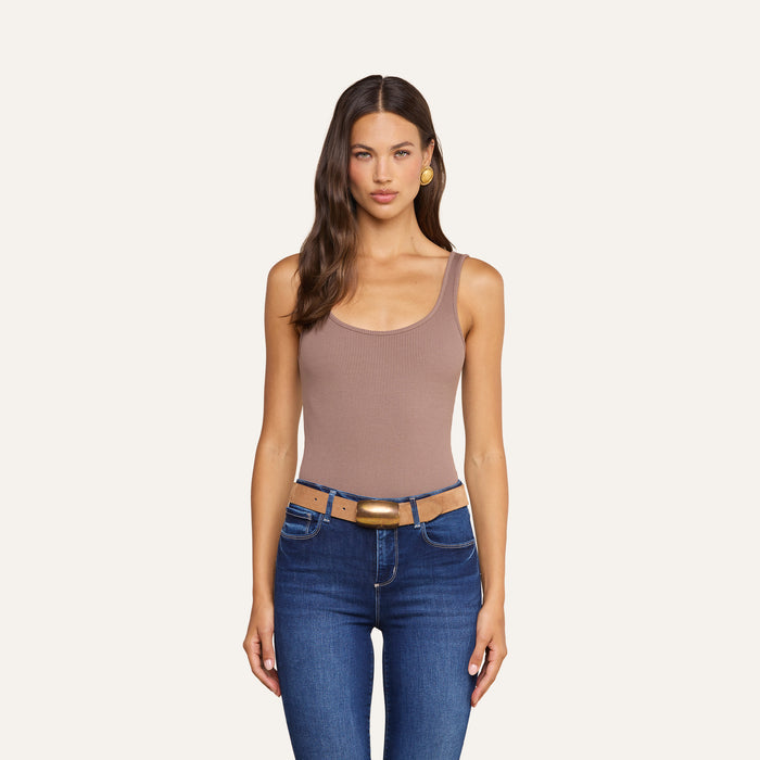 A woman with long brown hair wears the Nica Scoopneck Bodysuit, blue jeans, and a brown belt as she stands facing forward against a plain light background.