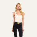 Wearing the Nica Scoopneck Bodysuit, a woman with long blonde hair pairs it with black pants and a black belt featuring a large gold buckle as she stands against a plain light background.