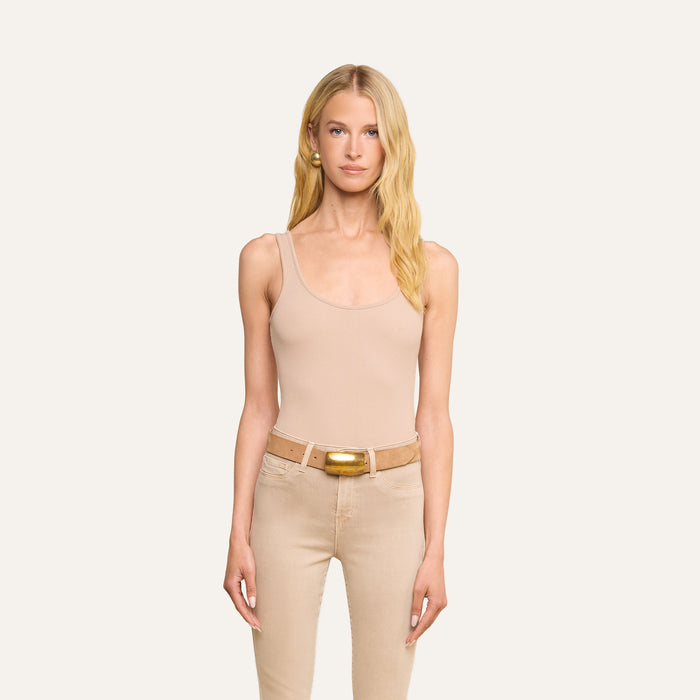 A woman with long blonde hair wears the Nica Scoopneck Bodysuit in beige, along with beige pants and a belt featuring a gold buckle, standing against a plain light background and facing forward with a neutral expression.
