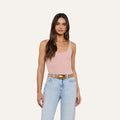 Woman with long brown hair wearing a light pink Nica Scoopneck Bodysuit with a sculpted fit, light blue high-waisted jeans, and a wide tan belt, standing against a plain white background.