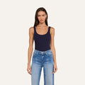 A woman with long brown hair wears the Nica Scoopneck Bodysuit in navy blue, styled with light blue high-waisted jeans, standing against a plain off-white background.