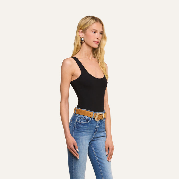 A woman with long blonde hair, wearing the Nica Scoopneck Bodysuit, blue jeans with a brown belt, and large round earrings stands against a plain light background.