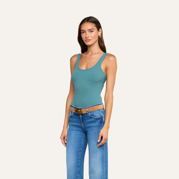 Woman standing against a plain background, wearing the Nica Scoopneck Bodysuit in teal, styled with blue jeans, a brown belt, and gold hoop earrings, with her hands by her sides.